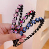 A hand holds a black rhinestone wave headband featuring pink and blue floral embellishments.