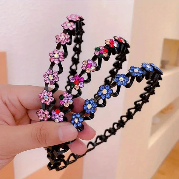 A hand holds a black rhinestone wave headband featuring pink and blue floral embellishments.