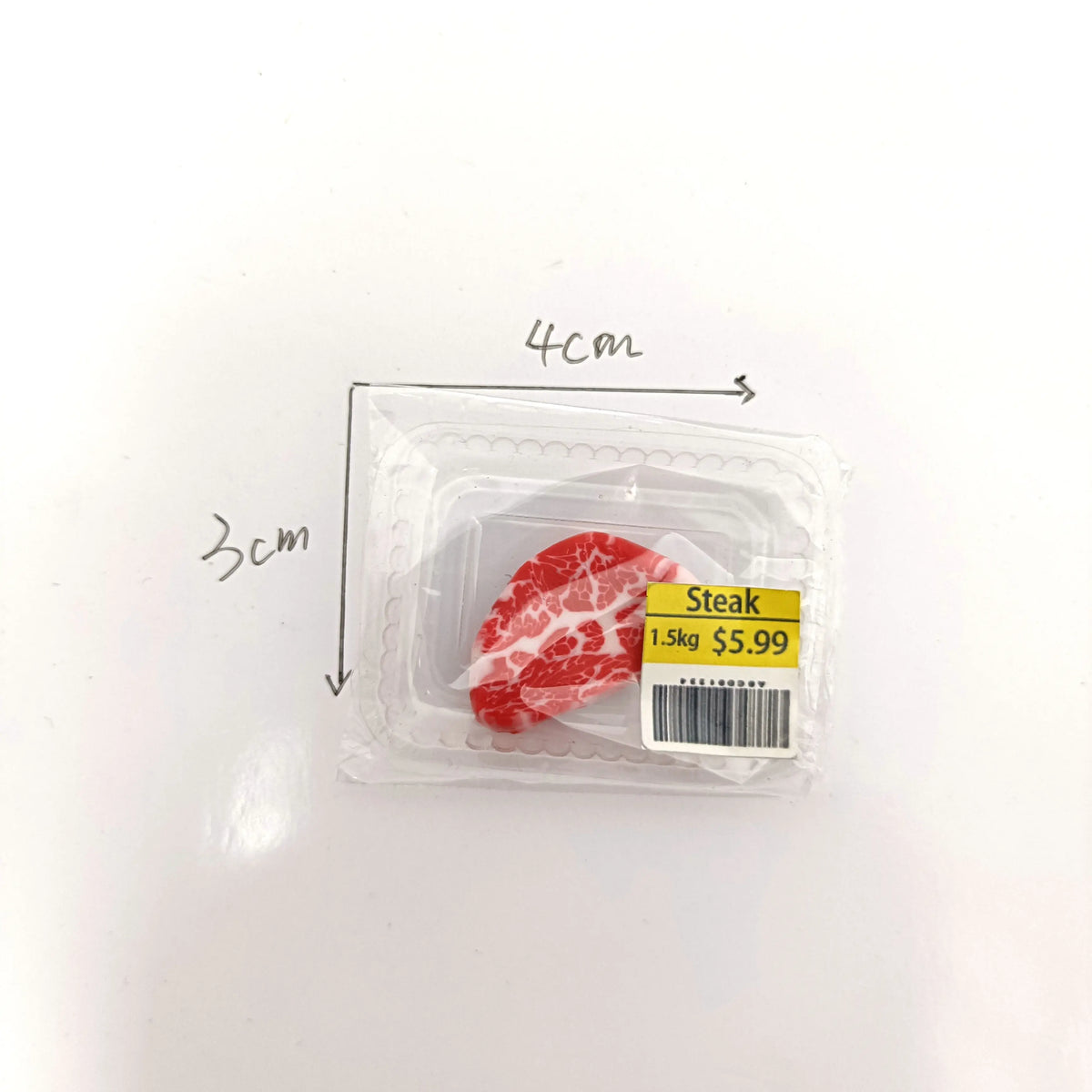 Un colis contenant un morceau de steak rouge étiqueté 1,5 kg pour 5,99 dollars, montré à côté d'une règle.