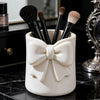 Organisateur de rangement en céramique blanche contenant plusieurs pinceaux de maquillage noirs sur une surface sombre.