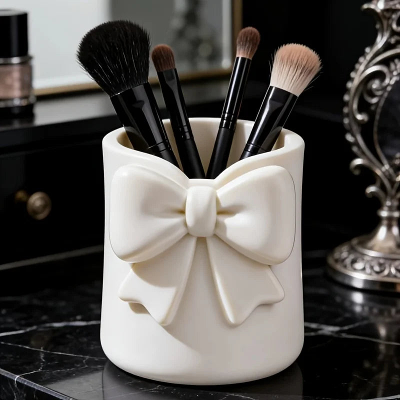 Organisateur de rangement en céramique blanche contenant plusieurs pinceaux de maquillage noirs sur une surface sombre.