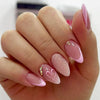 A hand displays pink flower almond press on nails with glitter and small gold accents.