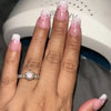 A hand displaying long, pink acrylic nails decorated with small floral designs, next to a white nail product packaging.