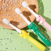 A set of pink and yellow cartoon dinosaur toothbrushes for kids resting on a wooden board with clear plastic beads.