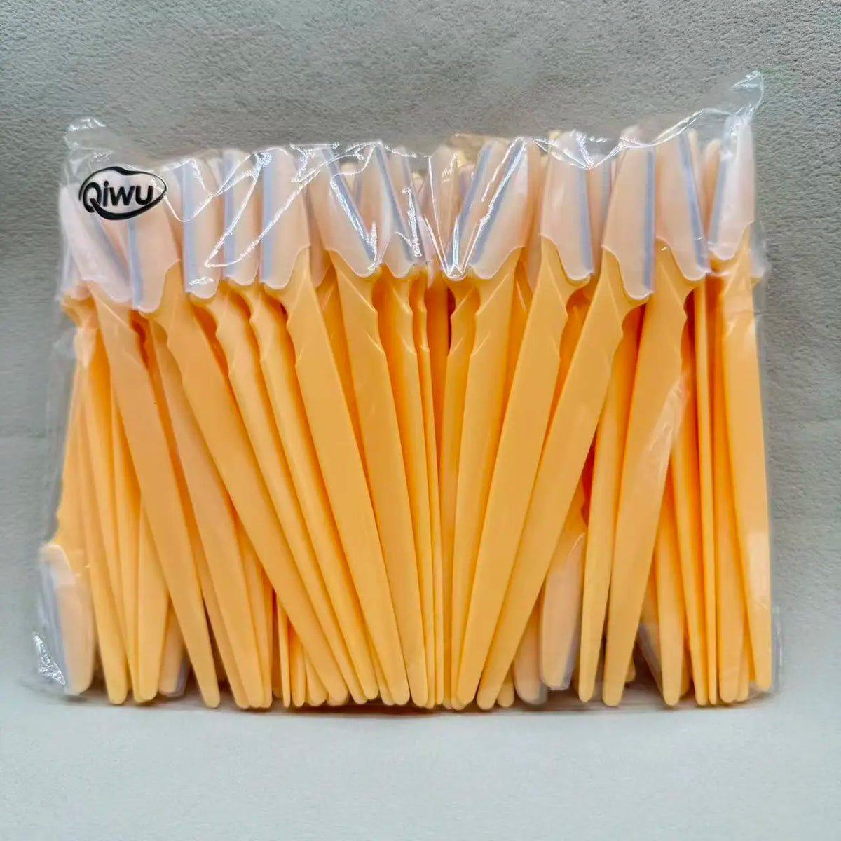 Un lot de ciseaux à sourcils orange, emballés dans du plastique transparent.