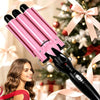 Un rizador de cabello triple barril de cerámica rosa junto a una mujer en un ambiente festivo navideño.