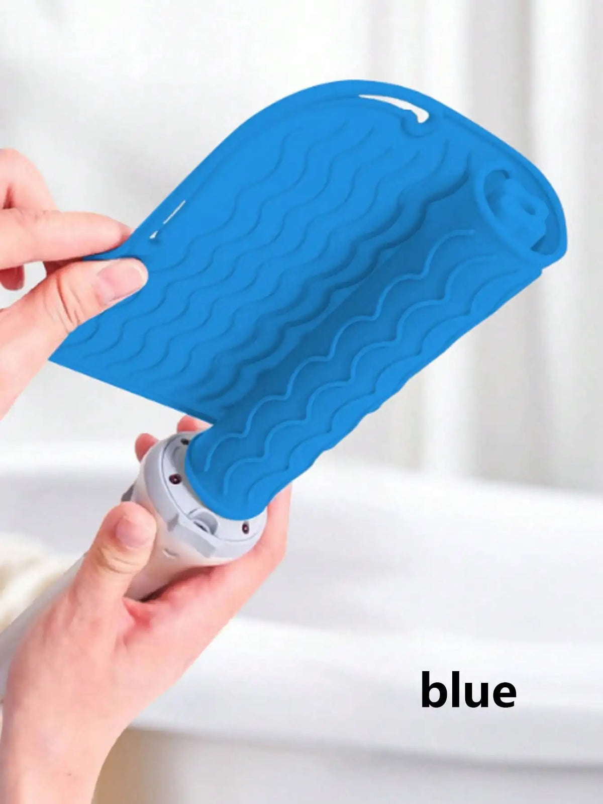 A hand holds a bright blue silicone heat resistant mat for hair styling tools.