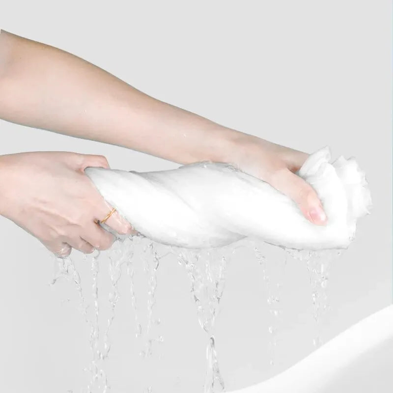 Una mano sostiene una toalla facial y de viaje blanca comprimida, con agua goteando.