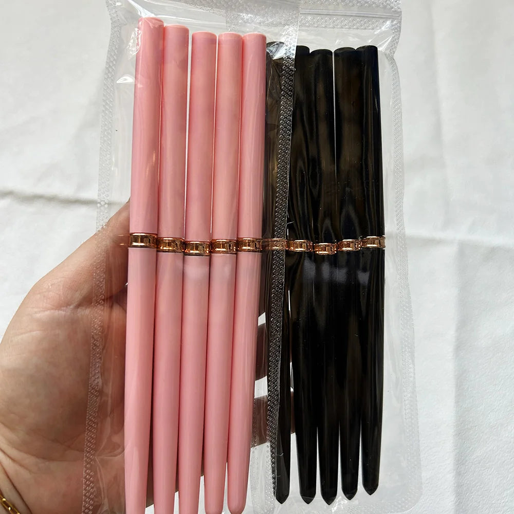Un set de pinceaux pour liner de nail art de précision, avec des poils roses et noirs et des accents dorés, tenu dans un pot 