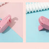A pink mini folding eyelash curler set resting on a light blue surface next to a white comb.