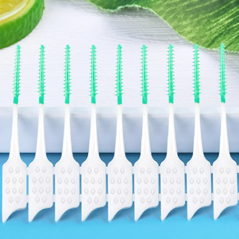 Un juego de hilo dental de silicona blanca con cerdas verdes, dispuestos en fila sobre una superficie azul claro.