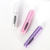 Three portable mini perfume refill sprays in silver, pink, and purple lying on a white surface.