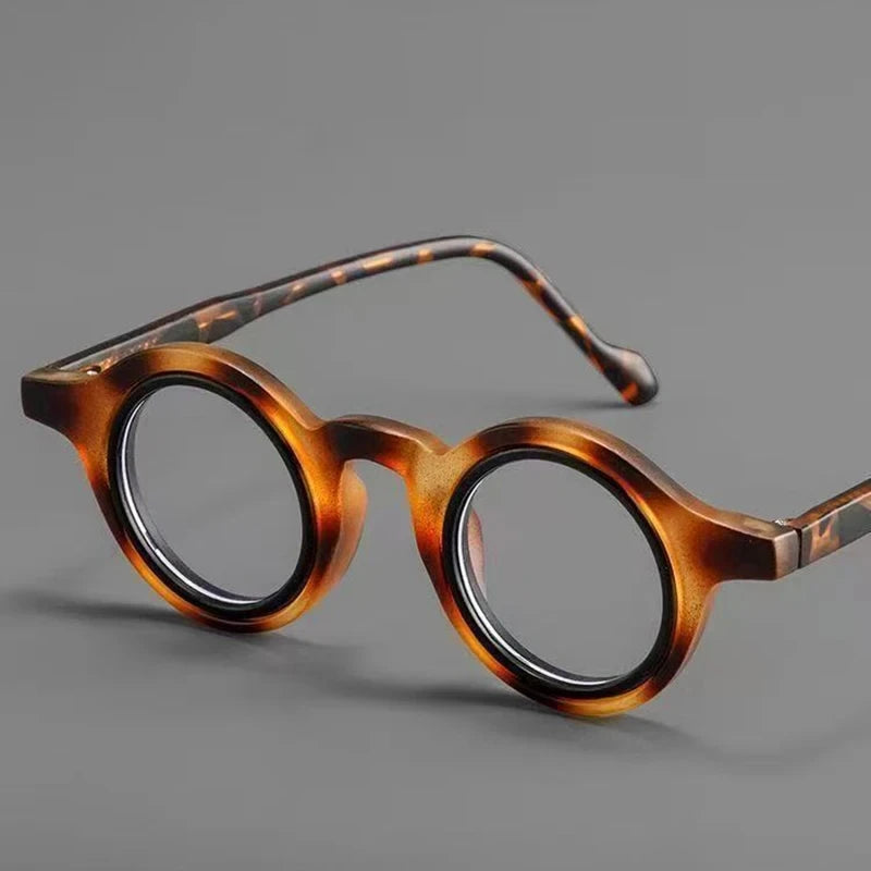 Une paire de lunettes de lecture transparentes réglables teintées de brun posées sur une surface grise.