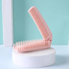 A pink portable folding hairbrush with anti-static bristles resting on a white stand.