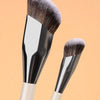 A pair of professional makeup brushes with silver ferrules and natural hair bristles against a light orange background.