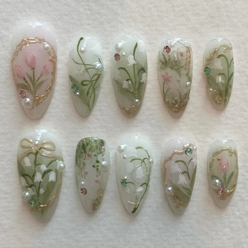 A set of 24 press-on fake nails featuring pink hearts, pearls, and green floral designs on a sheer white base.
