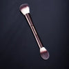 A professional double-ended makeup powder brush set with dark handles and fluffy bristles is shown against a dark background.