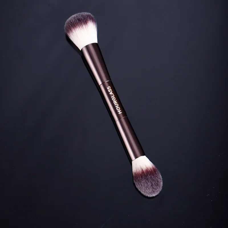 A professional double-ended makeup powder brush set with dark handles and fluffy bristles is shown against a dark background.