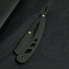 Couteau de rasage pliante antique noir avec poignée et lame, visible sur fond sombre.