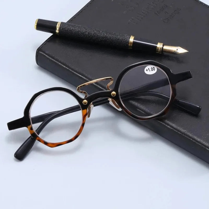 Une paire de lunettes rondes à monture noire posées sur un carnet sombre à côté d'un stylo or.