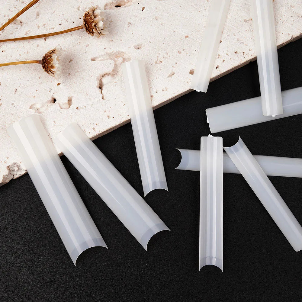 A set of clear acrylic press-on nails displayed on a light surface with dried floral elements.