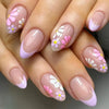 A close-up of a hand displaying press-on acrylic nails decorated with pink and white floral designs.