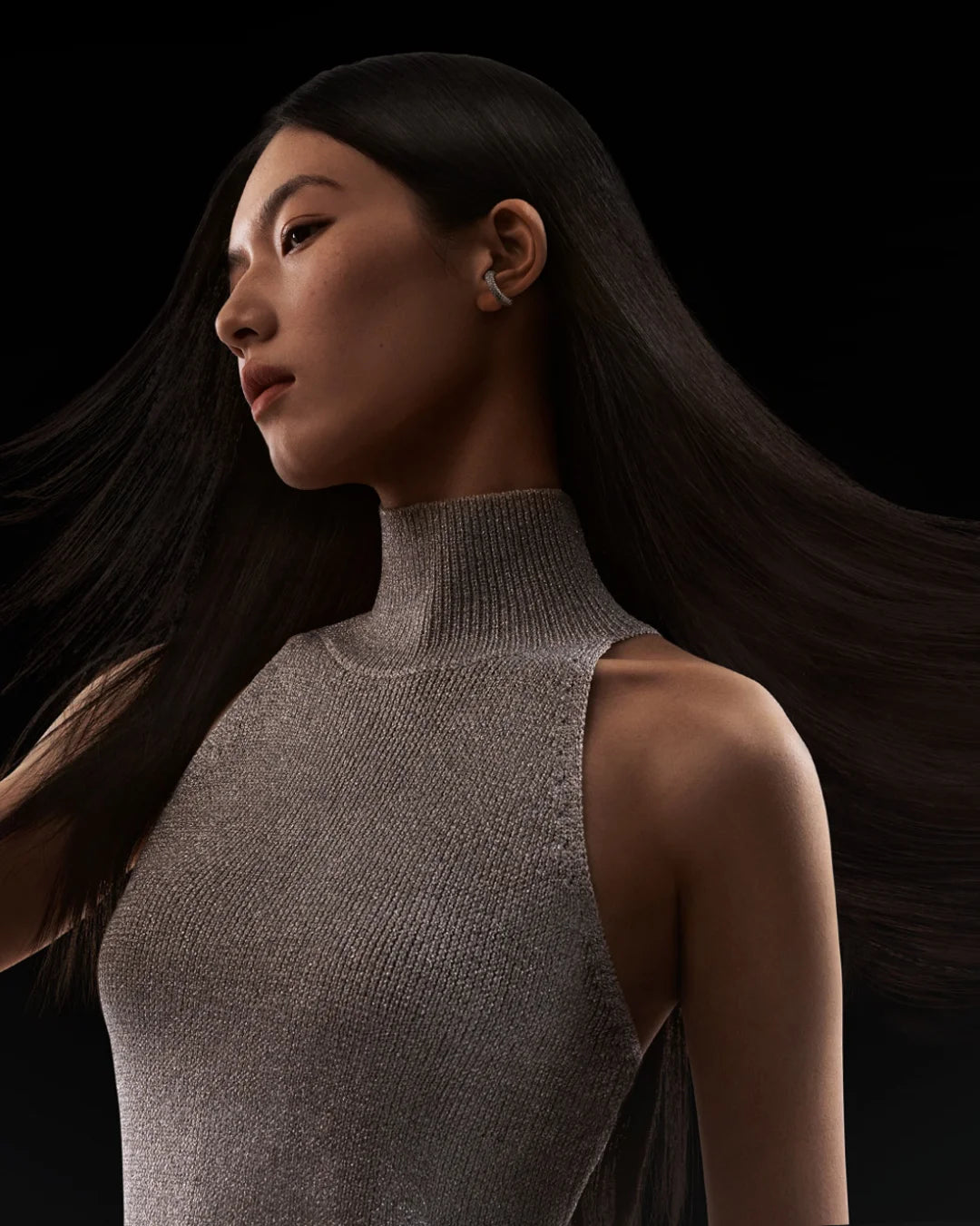 Model mit langem dunklem Haar trägt ein strukturiertes, hohes Kragen-Top und benutzt einen professionellen Hochgeschwindigkei