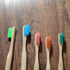 A collection of five bamboo toothbrushes in various colors including green blue pink orange and teal