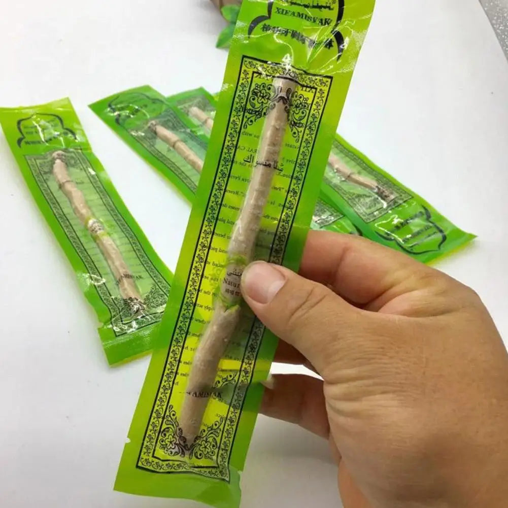 A hand holds a packet of traditional Miswak toothbrush for natural dental care, showing the wooden stick inside.