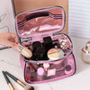 A hand is opening a clear pink cosmetic bag containing various makeup products and brushes.