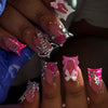 A close-up of a hand displaying nude pink press-on nails featuring leopard print and 3D silver charms.
