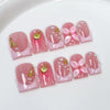 Un set de uñas postizas de flores rosa nude y perlas con acentos dorados sobre fondo blanco.