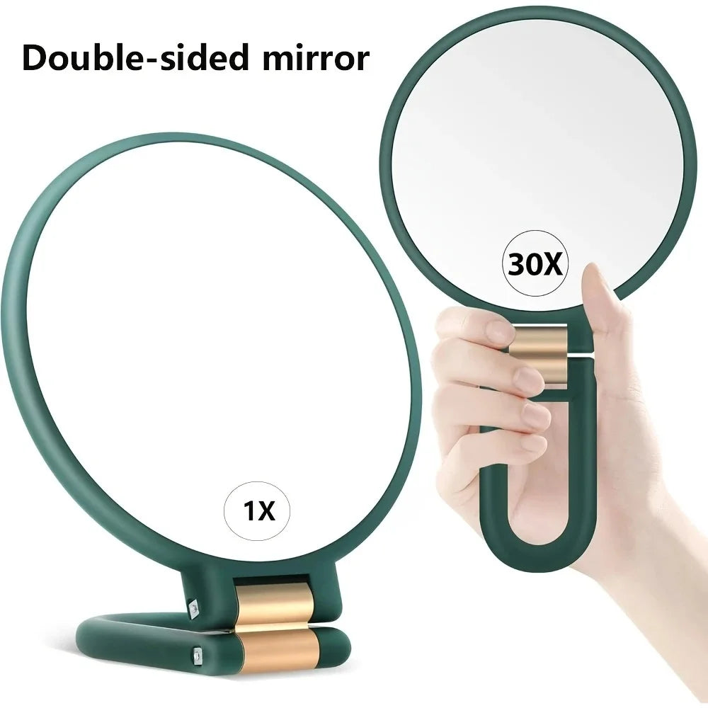 A double-sided magnifying mirror with a green frame and gold accents being held up to show a magnified reflection.