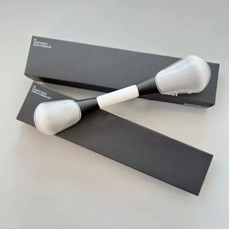 A pair of black and white dual-ended makeup brushes for foundation and contour displayed on a gray surface.