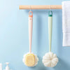 A pair of long-handle loofahs, one pink and one green, are hanging on a wooden rack against a light blue background.