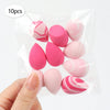 A hand holds a clear plastic bag containing ten pink and white reusable expandable makeup sponges.