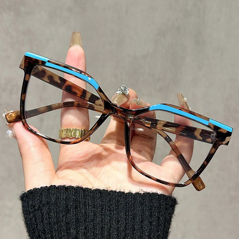 Una mano sostiene unas gafas de lectura marrones tortugas con monturas azules contra un fondo gris.