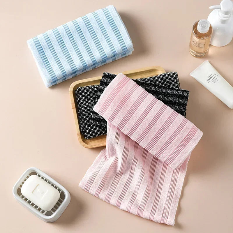 A pink striped exfoliating back scrubber bath towel is shown next to a blue striped towel and a white exfoliating soap bar.
