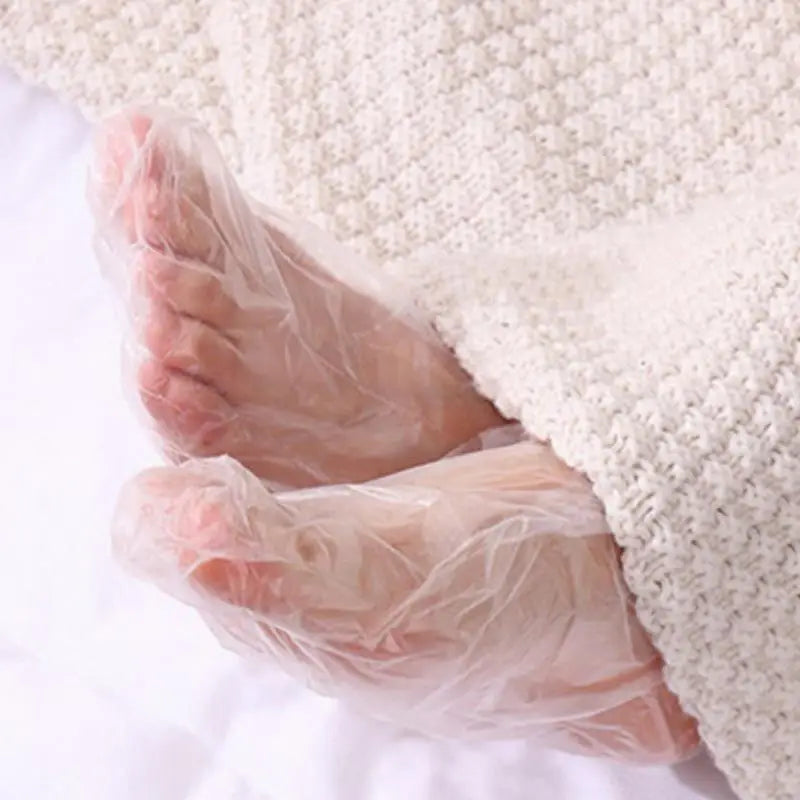 Chaussettes hydratantes pour les pieds jetables montrées sur le pied d'une personne, enveloppées dans du plastique transparen