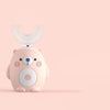 A pink electric toothbrush shaped like a bear with a clear silicone brush head against a light background.
