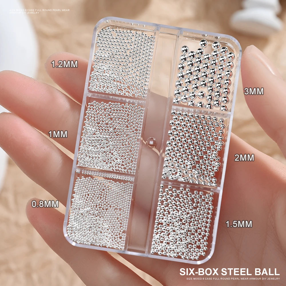 A clear box containing six different sizes of mixed stainless steel beads for nail art decorations