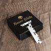 A black box containing a stainless steel single-sided razor blade is displayed on a wooden surface.