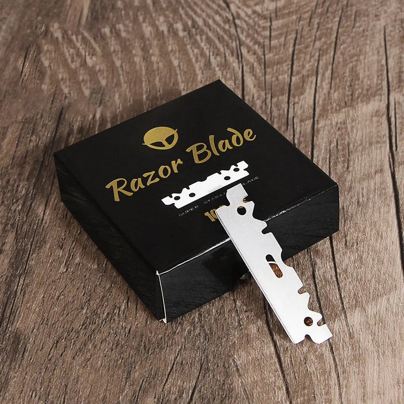 A black box containing a stainless steel single-sided razor blade is displayed on a wooden surface.