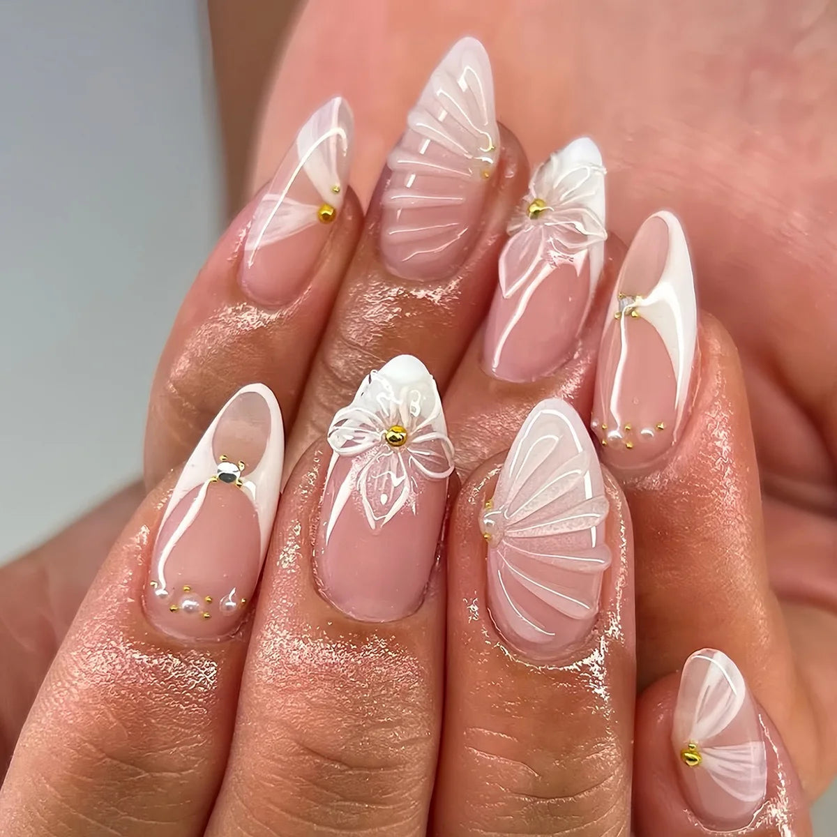 A hand displays a set of 24-piece almond press-on nails featuring delicate white and gold floral and butterfly designs.