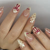 A close-up of a hand displaying pink heart pearl press-on fake nails with red accents on a light pink background.