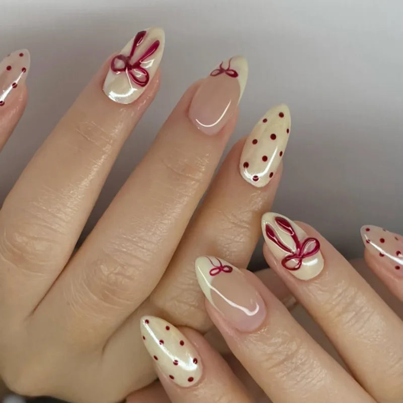 A close-up of a hand displaying pink heart pearl press-on fake nails with red accents on a light pink background.