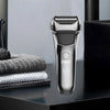 A silver electric shaver with a textured head is shown on a dark surface.
