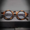 Une paire de lunettes de lecture claires à monture marron réglables posées sur une surface sombre.