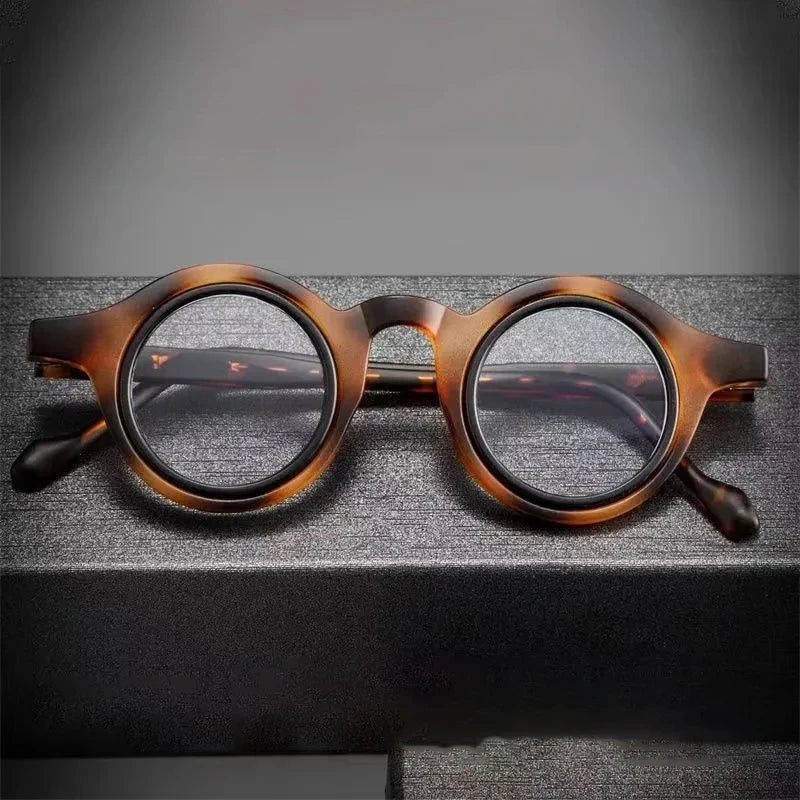 Une paire de lunettes de lecture claires à monture marron réglables posées sur une surface sombre.