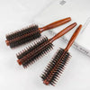 A pair of wooden natural boar bristle curling brushes resting on a white surface.
